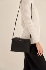 Profile view of model wearing the Oroton Elsie Nylon Zip Top Crossbody in Black and Nylon And Pebble Leather for Women