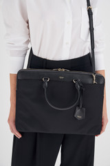 Profile view of model wearing the Oroton Inez Nylon 13" Slim Laptop Bag in Black and Nylon/ Shiny Soft Saffiano for Women