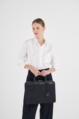 Profile view of model wearing the Oroton Inez Nylon 13" Slim Laptop Bag in Black and Nylon/ Shiny Soft Saffiano for Women