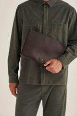 Profile view of model wearing the Oroton Lucas 13" Laptop Cover in Chocolate/Black and Pebble Leather for Men