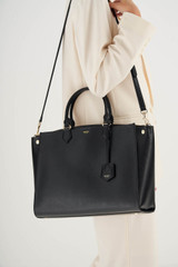 Profile view of model wearing the Oroton Inez 15" Zip Around Worker Tote in Black and Shiny Soft Saffiano for Women