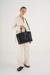 Profile view of model wearing the Oroton Inez 15" Zip Around Worker Tote in Black and Shiny Soft Saffiano for Women