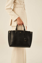 Profile view of model wearing the Oroton Inez 13" Zip Around Worker Tote in Black and Shiny Soft Saffiano for Women