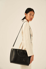 Profile view of model wearing the Oroton Inez 13" Zip Around Worker Tote in Black and Shiny Soft Saffiano for Women