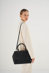 Profile view of model wearing the Oroton Inez Medium City Tote in Black and Shiny Soft Saffiano for Women
