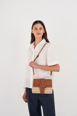 Profile view of model wearing the Oroton Frida Collectable Medium Satchel in Natural/Brandy and Woven Straw and Smooth Leather for Women