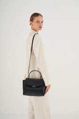 Profile view of model wearing the Oroton Inez Medium Satchel in Black and Shiny Soft Saffiano for Women