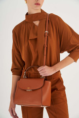 Profile view of model wearing the Oroton Inez Medium Satchel in Cognac and Shiny Soft Saffiano for Women