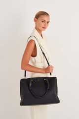 Profile view of model wearing the Oroton Anika 15" Day Bag in Black and Pebble leather for Women