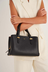 Profile view of model wearing the Oroton Anika Small Day Bag in Black and Pebble leather for Women