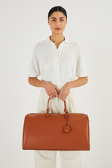 Profile view of model wearing the Oroton Inez Weekender in Cognac and Saffiano Leather for Women