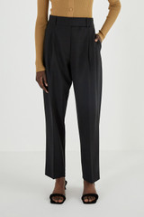 Profile view of model wearing the Oroton Pleat Pant in Black and 53% Polyester 42% Wool 5% Elastane for Women