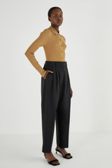 Profile view of model wearing the Oroton Pleat Pant in Black and 53% Polyester 42% Wool 5% Elastane for Women