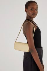 Profile view of model wearing the Oroton Muse Apple Mini Baguette in Almond and AppleSkin™: 20% GRS (Global Recycled Standard) Polyester, 16% GRS Cotton, 26% Apple Waste, 38% Polyurethane for Women