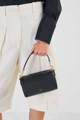 Profile view of model wearing the Oroton Thea Small Barrel Bag in Black and Smooth Leather for Women
