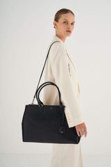 Profile view of model wearing the Oroton Inez 15" City Tote in Black and Shiny Soft Saffiano for Women