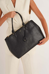 Profile view of model wearing the Oroton Inez 15" City Tote in Black and Shiny Soft Saffiano for Women