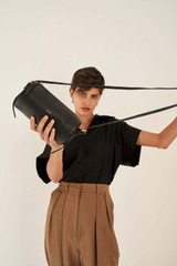 Profile view of model wearing the Oroton Margot Drum Bag in Black and Pebble Leather for Women