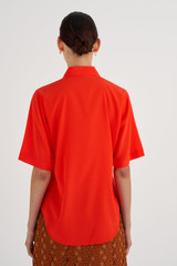 Profile view of model wearing the Oroton Short Sleeve Fluid Shirt in True Red and 92% Silk, 8% Spandex for Women