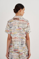Profile view of model wearing the Oroton Short Sleeve Label Print Camp Shirt in Soft Cream and 100% Silk for Women
