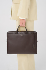 Profile view of model wearing the Oroton Muse Apple 15" Slim Laptop Bag in Dark Chocolate and Vegan leather for Women