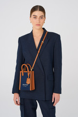 Profile view of model wearing the Oroton Muse Canvas Mini Top Handle in Yacht Blue/Brandy and Canvas and leather trims for Women
