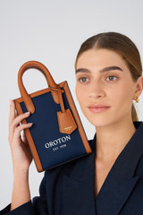 Profile view of model wearing the Oroton Muse Canvas Mini Top Handle in Yacht Blue/Brandy and Canvas and leather trims for 