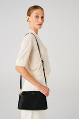 Profile view of model wearing the Oroton Anika Zip Top Crossbody in Black and Pebble leather for Women