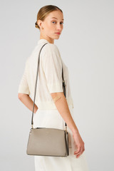 Profile view of model wearing the Oroton Anika Zip Top Crossbody in Oyster and Pebble leather for Women