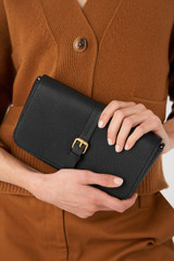 Profile view of model wearing the Oroton Dylan Clutch Crossbody in Black and Pebble leather, smooth leather trims for Women