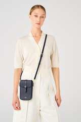 Profile view of model wearing the Oroton Dylan Buckle Phone Crossbody in Dark Navy and Pebble leather, smooth leather trims for Women