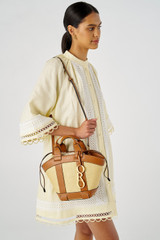 Profile view of model wearing the Oroton Harper Small Tote in Natural/Brandy and Woven straw with smooth leather trims for Women