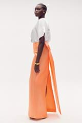 Profile view of model wearing the Oroton Drape Back Skirt in Bright Melon and 85% polyester, 15% silk for Women