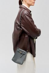 Profile view of model wearing the Oroton Margot Tiny Bucket Bag in Dark Slate and Pebble leather for 
