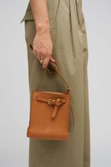 Profile view of model wearing the Oroton Margot Tiny Bucket Bag in Dark Camel and Smooth Leather Lining for Women