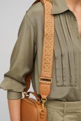 Profile view of model wearing the Oroton Logo Bag Strap in Dark Camel and Smooth Leather And Webbing for Women