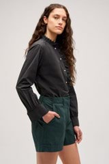 Profile view of model wearing the  Hazel Ruffle Blouse in Washed Black and Made from 100% poplin cotton  for Men