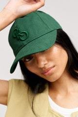 Profile view of model wearing the Oroton Oro Logo Cap in Villa Green and High-quality 100% cotton   for Women