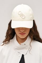 Profile view of model wearing the Oroton Oro Logo Cap in Antique White and High-quality 100% cotton   for Women