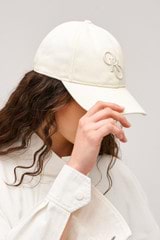 Profile view of model wearing the Oroton Oro Logo Cap in Antique White and High-quality 100% cotton   for Women