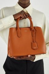 Profile view of model wearing the Oroton Muse Small Three Pocket Day Bag in Cognac and Saffiano And Smooth Leather for Women