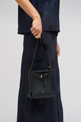 Profile view of model wearing the Oroton Margot Tiny Bucket Bag in Black and Pebble leather for Women