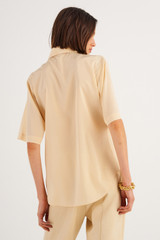 Profile view of model wearing the Oroton Short Sleeve Fluid Blouse in Creamed Honey and 92% Silk 8% Spandex for Women